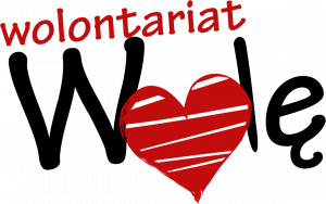 Logotyp Wolontariat Wolę. Czerwony napis wolontariat znajduje się powyżej czarnego napisu WOLĘ przy którym literka O zastąpiona jest czerwonym sercem